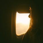 a woman looking out an airplane window at the sunset