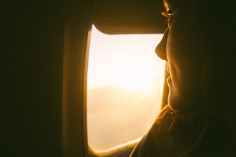 a woman looking out an airplane window at the sunset